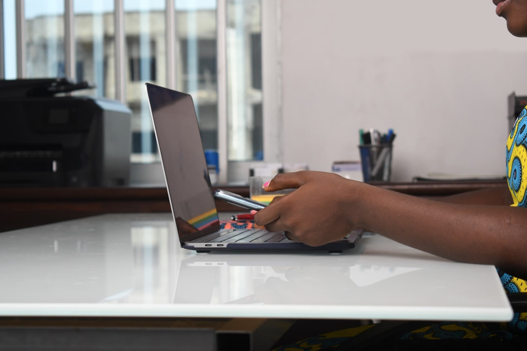A person at a white desk working on a laptop, phone in hand